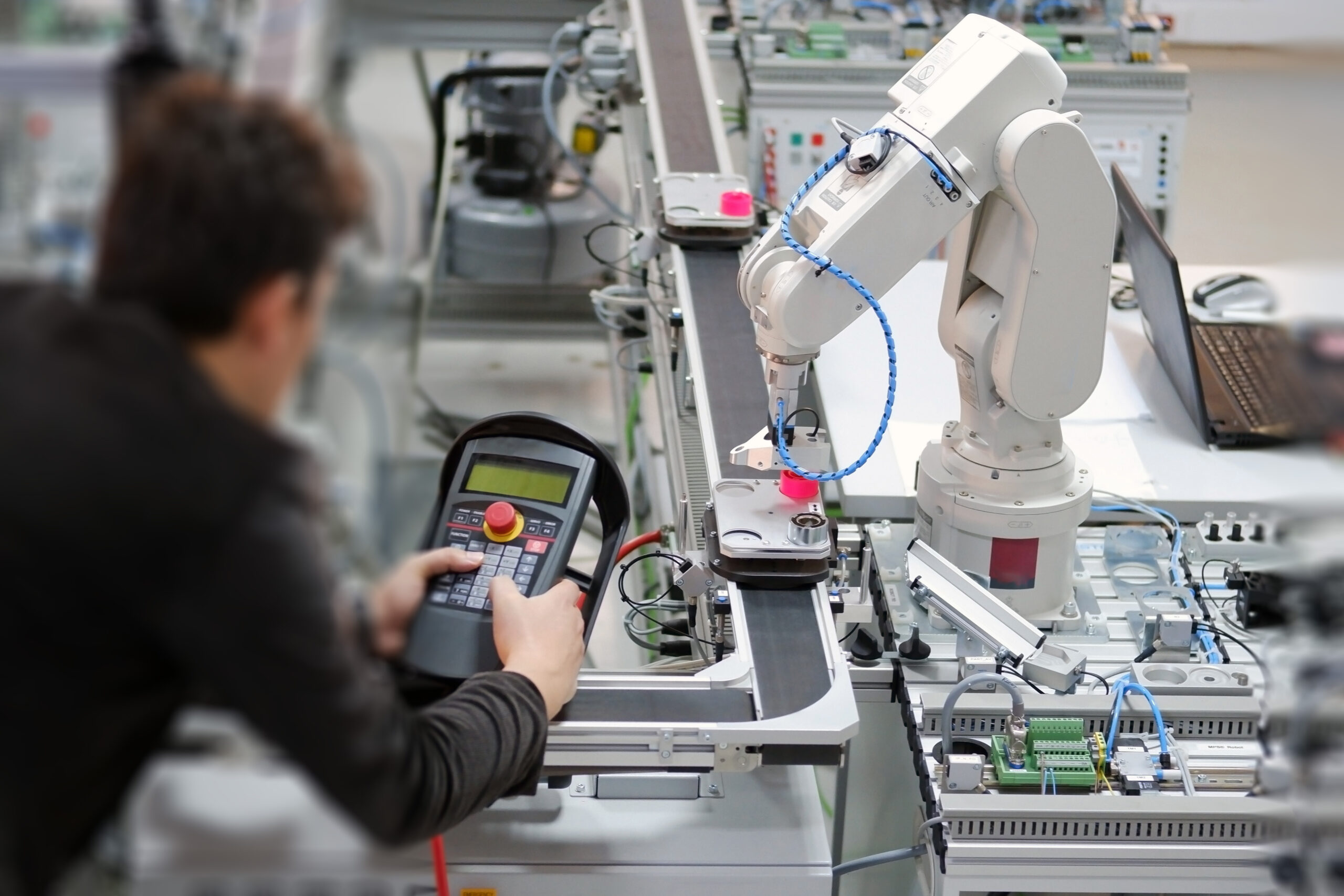 Man is holding teach panel to control a robotic arm which is int